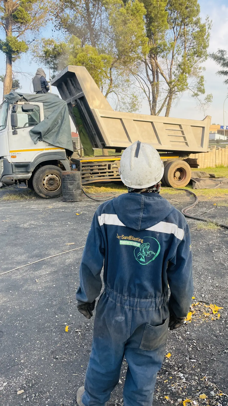 Za-SandBlasting operator in branded overalls and hard hat beside a tipper truck