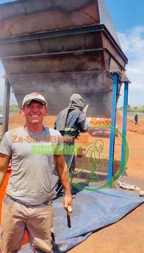 Smiling Za-SandBlasting team member in front of a large steel hopper while an operator blasts it on-site