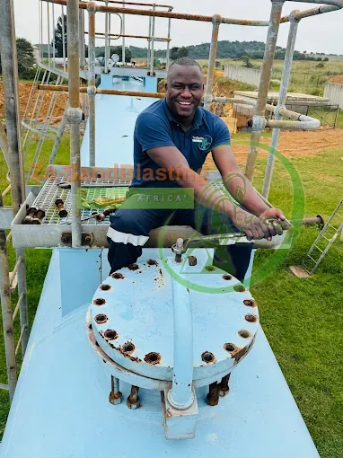 Technician smiling beside a blasted water tank flange